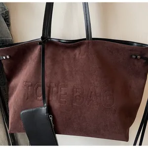 Détail du sac cabas en suédine avec lettrage embossé et pochette en cuir noir