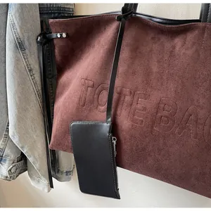 Détail d'un cabas en daim marron foncé avec lettrage embossé et accessoire en cuir noir