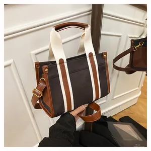 Detail of canvas and leather tote bag featuring white stripes and gold-tone hardware