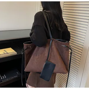 Détail d'un grand cabas en daim marron avec lettrage texturé et une petite pochette