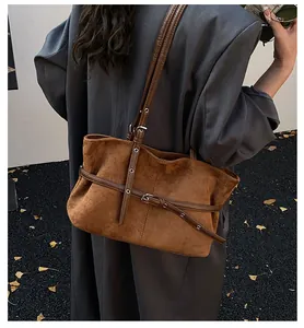 Détail du sac cabas en daim caramel avec boucles de ceinture porté sur un blazer gris