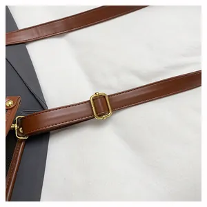 Detail of adjustable brown leather shoulder strap with gold metal buckle on a canvas tote