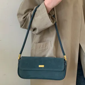 Sac baguette vintage en daim vert foncé avec boucle dorée sur un manteau beige