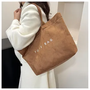 Close-up of brown suede tote bag with white text print and slim shoulder straps