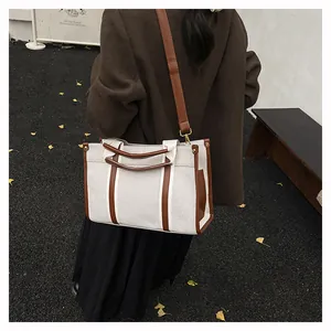 Outdoor shot of beige canvas tote with brown leather trim and adjustable strap detail