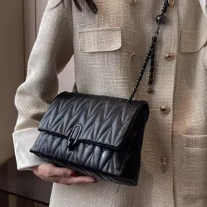 Elegant black matelassé chain handbag with metal buckle worn on tweed jacket
