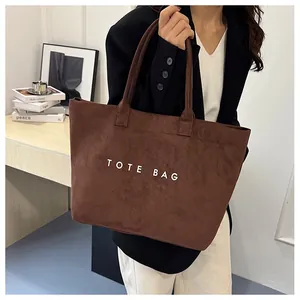 Close-up of brown suede tote bag featuring white printed TOTE BAG text with long handles