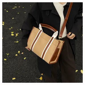 Detail of canvas tote bag with brown leather trim and white vertical webbing decoration