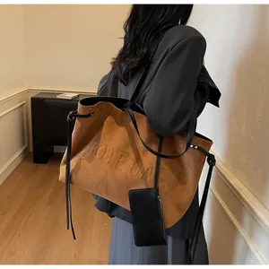 Détail d'un sac cabas en daim marron avec logo embossé et bandoulière en cuir