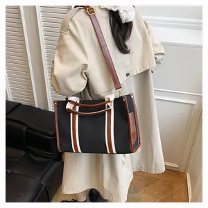 Detail of black canvas tote bag with brown leather trim and adjustable crossbody strap