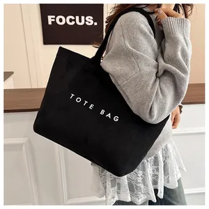 Detailed view of black canvas tote bag featuring white TOTE BAG print on model
