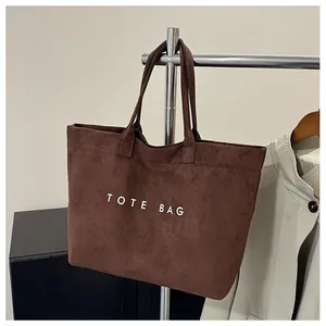 Detail of a dark brown suede tote bag featuring white printed letters and a metal hanger