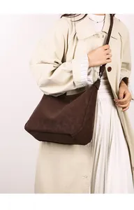 Detail of dark brown suede crossbody bag styled with a beige trench coat on a model