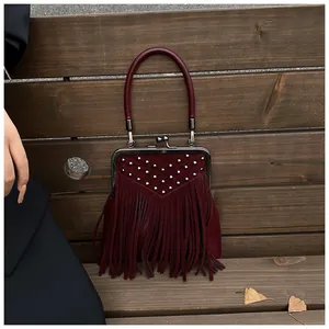 Close-up of burgundy suede handbag featuring silver rivets, long tassels and retro clasp