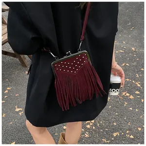 Detail of burgundy suede crossbody bag with metal rivets, fringe, and vintage clasp
