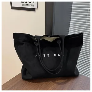 Close-up of black suede tote bag with white TOTE BAG lettering on a wooden desk