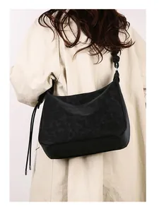 Detail of vintage black suede crossbody bag with knotted strap on a beige trench coat