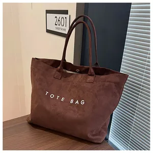 Detail of a brown suede tote bag with white TOTE BAG text on a dark wooden table