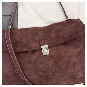 Detail of dark brown suede shoulder bag with silver metal buckle and white stitching