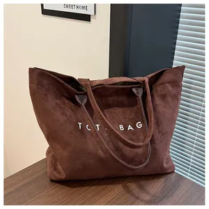 Detail of a brown faux suede tote bag featuring a minimalist white TOTE BAG print