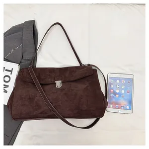 Detailed view of dark brown suede shoulder bag with silver push-lock on white background