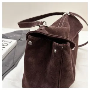 Close-up of brown suede shoulder bag featuring silver buckle and vintage stitching details