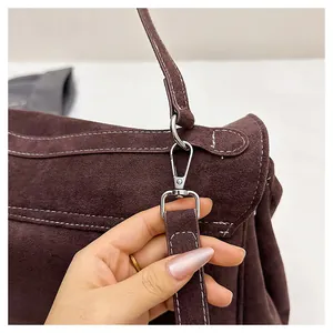 Detailed close-up of the silver lobster clasp on a dark brown suede shoulder bag