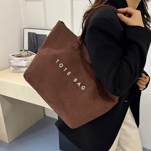 Brown suede minimalist tote bag with large white logo for women in office casual setting
