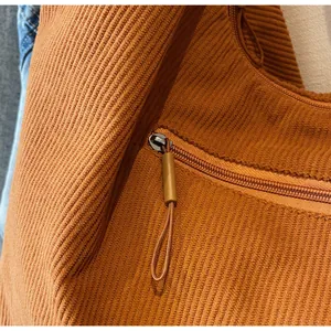 Detailed macro view of the caramel corduroy fabric and zipper pocket of a tote bag