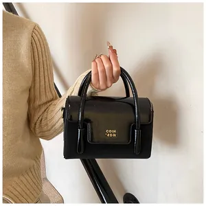 Detail of a black patent leather handbag with gold logo and elegant pleated texture