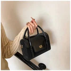 Detail of glossy black patent leather handbag with gold metal lettering and top handle