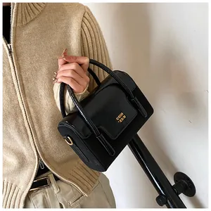Detail of glossy black square bag with gold COIH 2DN logo and metallic hardware