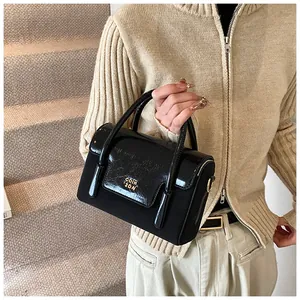 Detail of a chic black textured handbag with gold logo and glossy patent leather handle