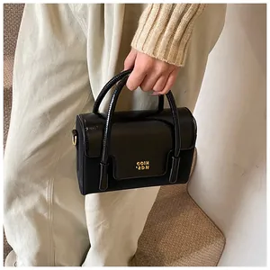 Detail shot of a black leather handbag with gold metal logo and dual handle structure