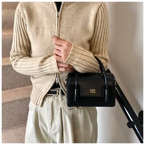Detailed close-up of a glossy black crossbody bag with gold logo on beige knitwear