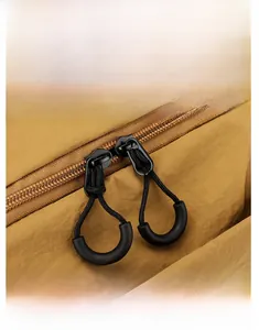 Detail shot of the smooth double zippers with black knotted cords on the brown nylon backpack