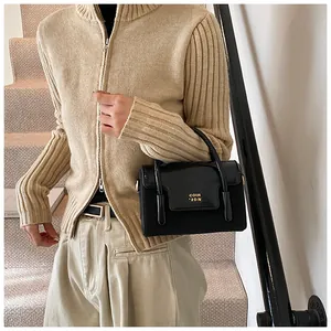 Fashionable black glossy crossbody bag with gold logo shown in a chic street style outfit