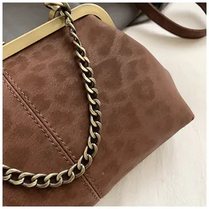 Gros plan du fermoir baiser en bronze et de la chaîne métallique sur le sac vintage brun