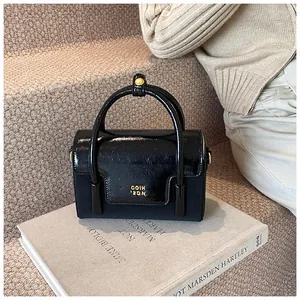 Close-up of black glossy patent leather handbag with gold logo on white art book