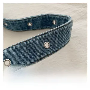 Detail of light blue denim shoulder strap with silver metal eyelets and double stitching