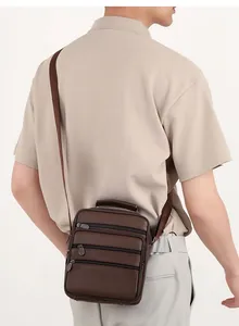 Rear view of a man carrying a brown leather shoulder bag with multiple zippered pockets