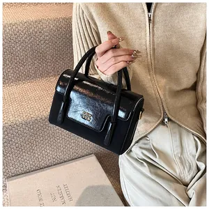 Detail of black faux leather handbag with gold metal logo and flap closure in warm lighting