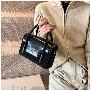 Detailed close-up of a black matte and patent leather handbag with a gold logo