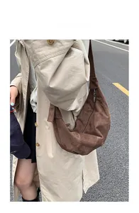 Outdoor street view showing the large brown suede hobo bag styled with a trench coat