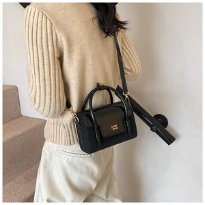 Close-up of black glossy small square bag with gold COIH 2DN text and top handle strap