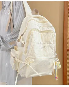 Dettaglio dello zaino bianco crema con ricamo e fiocchi decorativi sui lati