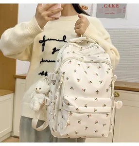 Detail of floral beige backpack showing side buckle straps and a cute plush bear charm