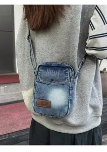Detail of casual denim crossbody bag with brown leather logo patch and front pocket