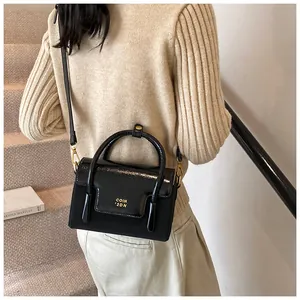 Close-up of black patent leather crossbody bag with gold hardware and logo on flap