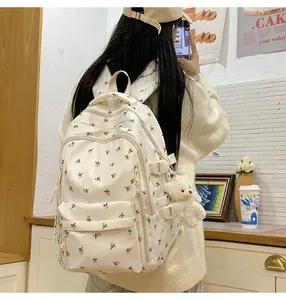 Detail of floral canvas backpack featuring pink flower patterns and a plush bear charm